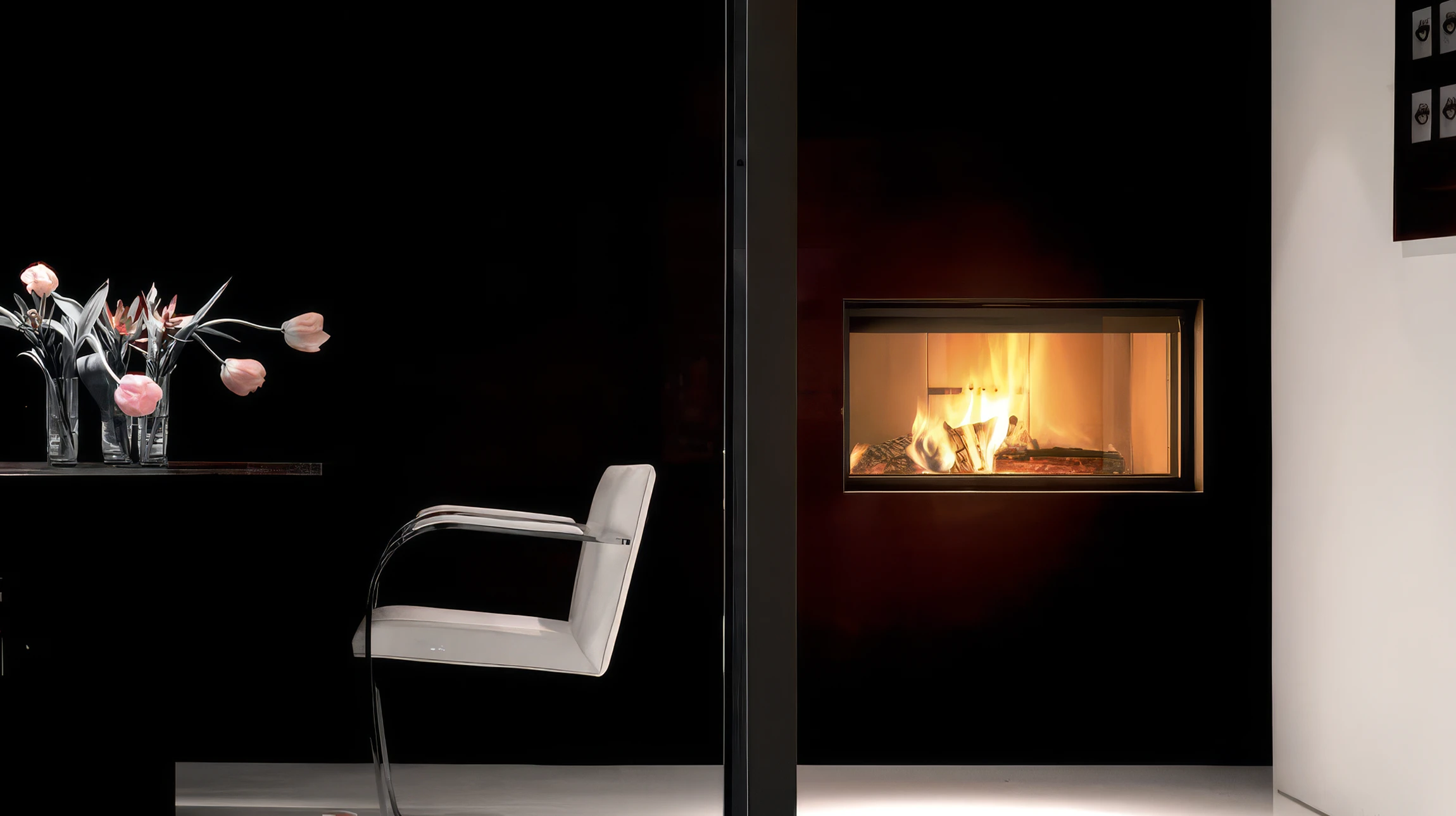 Intérieur moderne avec cheminée encastrée noire allumée dans mur gris, fauteuil velours vert olive, parquet bois clair, plantes vertes décoratives sur manteau cheminée blanc